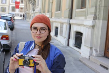 Şık hippi elbiseli, klasik kulaklıklı ve şehir caddesinde film kamerası olan güzel bir kadının portresi.