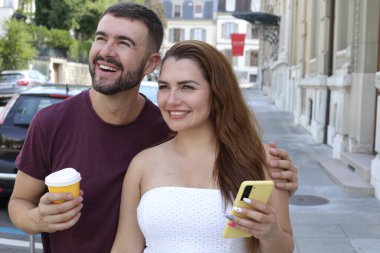 Genç mutlu çiftin portresi, kağıt bardak kahve ve akıllı telefonla birlikte şehir caddesinde.