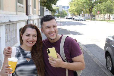 Genç mutlu çiftin portresi, kağıt bardak kahve ve akıllı telefonla birlikte şehir caddesinde.