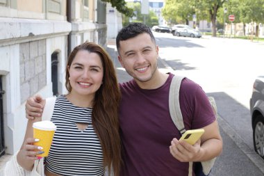 Genç mutlu çiftin portresi, kağıt bardak kahve ve akıllı telefonla birlikte şehir caddesinde.