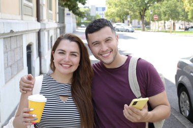 Genç mutlu çiftin portresi, kağıt bardak kahve ve akıllı telefonla birlikte şehir caddesinde.