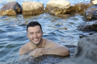 Kayalık deniz kıyısında suda poz veren yakışıklı genç adamın yakın plan portresi.
