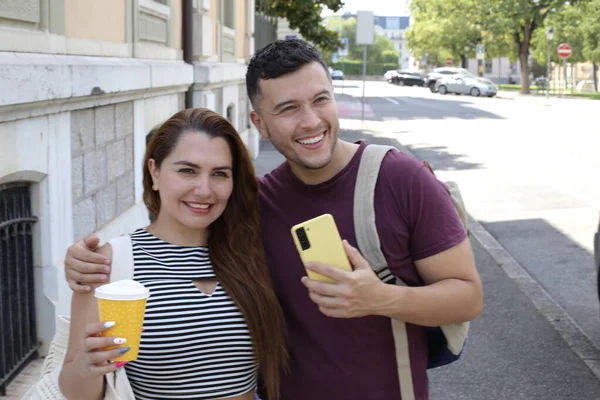 Genç mutlu çiftin portresi, kağıt bardak kahve ve akıllı telefonla birlikte şehir caddesinde.