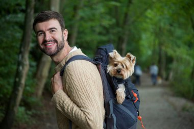Sırt çantasında sevimli köpeğiyle gezen yakışıklı, mutlu genç adamın portresi.