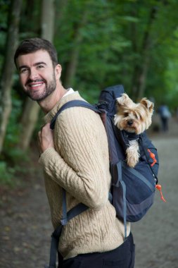 Sırt çantasında sevimli köpeğiyle gezen yakışıklı, mutlu genç adamın portresi.