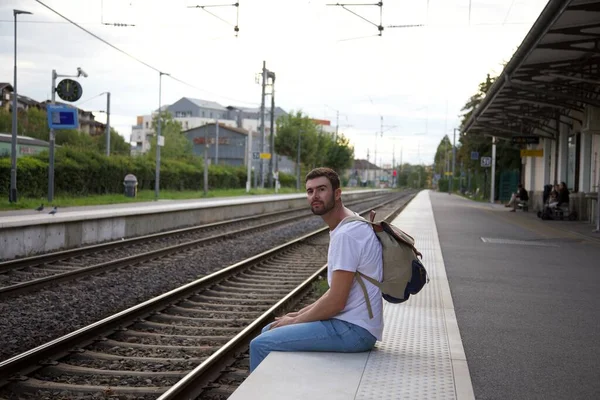 英俊快乐的年轻人背着背包在车站等火车的肖像 — 图库照片