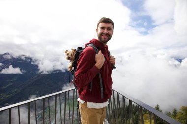 Sırt çantasında sevimli köpeğiyle gezen yakışıklı, mutlu genç adamın portresi.