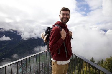 Sırt çantasında sevimli köpeğiyle gezen yakışıklı, mutlu genç adamın portresi.