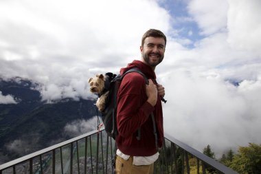 Sırt çantasında sevimli köpeğiyle gezen yakışıklı, mutlu genç adamın portresi.