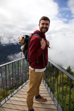 Sırt çantasında sevimli köpeğiyle gezen yakışıklı, mutlu genç adamın portresi.