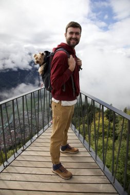 Sırt çantasında sevimli köpeğiyle gezen yakışıklı, mutlu genç adamın portresi.