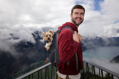 Sırt çantasında sevimli köpeğiyle gezen yakışıklı, mutlu genç adamın portresi.