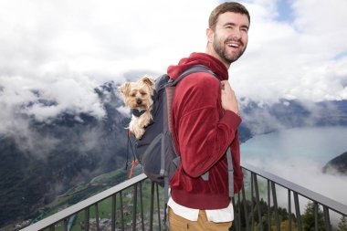 Sırt çantasında sevimli köpeğiyle gezen yakışıklı, mutlu genç adamın portresi.