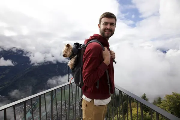 Sırt çantasında sevimli köpeğiyle gezen yakışıklı, mutlu genç adamın portresi.