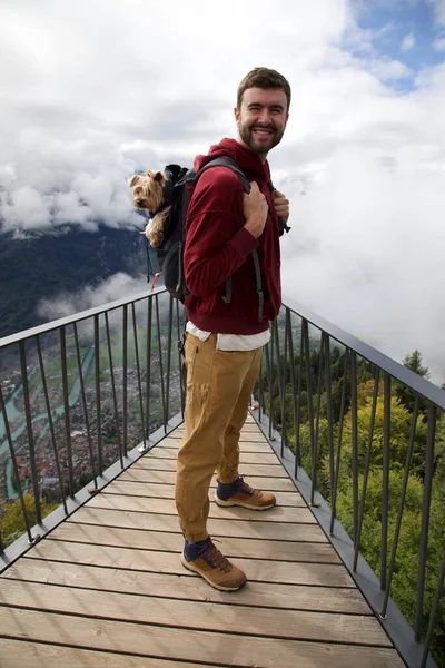 Sırt çantasında sevimli köpeğiyle gezen yakışıklı, mutlu genç adamın portresi.