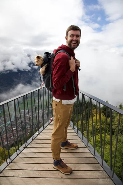 Sırt çantasında sevimli köpeğiyle gezen yakışıklı, mutlu genç adamın portresi.