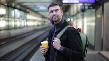 Tren istasyonunda elinde bir fincan kağıt kahveyle yakışıklı bir gencin yakın plan portresi.