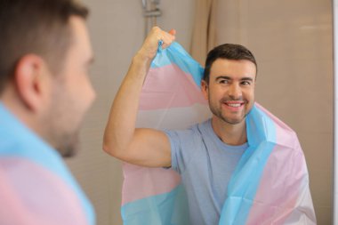 Banyoda aynanın önünde transseksüel bayraklı yakışıklı bir genç portresi.