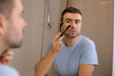 Yakışıklı bir gencin portresi. Banyo da aynanın önünde sakalını ip tıraşıyla tıraş ediyor.