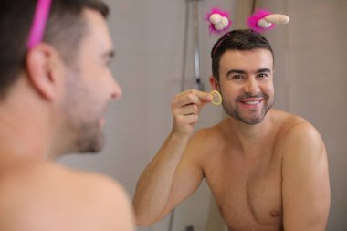 Banyoda aynanın önünde prezervatif tutan yakışıklı bir gencin portresi.
