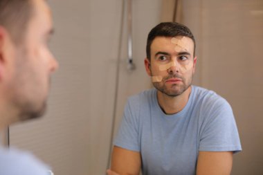 Banyoda aynanın önünde yüzü bandajlı yakışıklı genç adamın portresi.