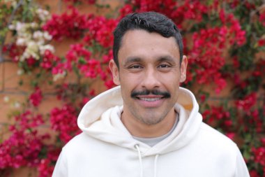 Beyaz kapüşonlu bıyıklı, kırmızı çiçeklerin önünde gülümseyen yakışıklı İspanyol adamın portresi.