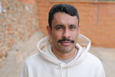 Beyaz kapüşonlu bıyıklı, kameraya bakan yakışıklı İspanyol adamın portresi.