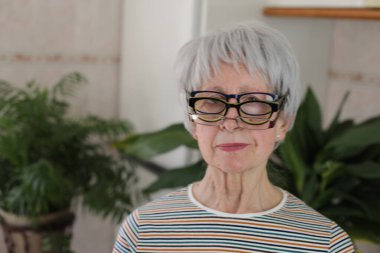 Evde bir yığın gözlüğü olan komik, olgun, gri saçlı bir kadının portresi.