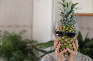 Olgun gri saçlı bir kadının portresi. Elinde komik bir ananas ve gözlüklü bir kadın.