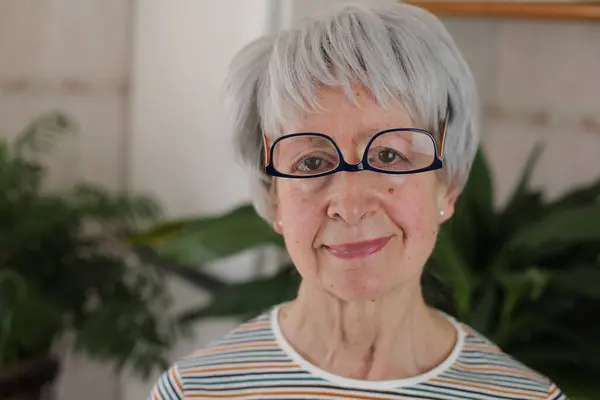 stock image portrait of mature grey haired woman with upside down eyeglasses on face at home