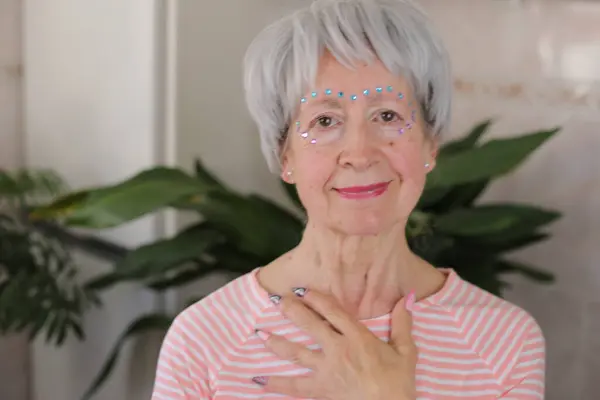 stock image portrait of mature grey haired woman with glossy gems on face and painted nails at home