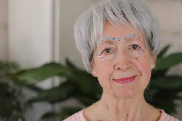 stock image portrait of mature grey haired woman with glossy gems on face at home