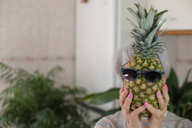 Güneş gözlüklü ananas tutan son sınıf kadını..