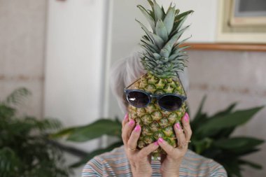 Güneş gözlüklü ananas tutan son sınıf kadını..