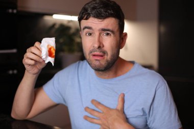 Arka planda kan lekesi olan bir adam öksürüyor.