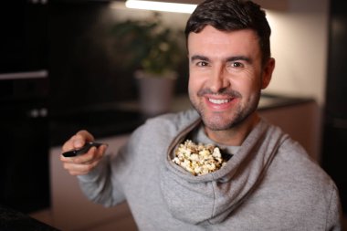 Kapüşonlu kapüşonlu komik adam televizyon izlerken patlamış mısırını depoladı.