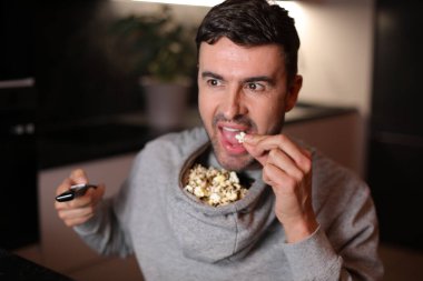 Kapüşonlu kapüşonlu komik adam televizyon izlerken patlamış mısırını depoladı.