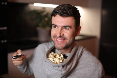 Kapüşonlu kapüşonlu komik adam televizyon izlerken patlamış mısırını depoladı.