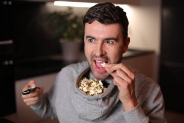 Kapüşonlu kapüşonlu komik adam televizyon izlerken patlamış mısırını depoladı.