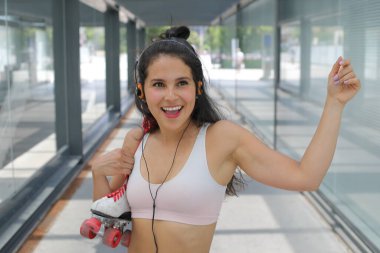 Kulaklıklı güzel bir genç kadının portresi ve sokakta rol patenleriyle müzik dinlemek.