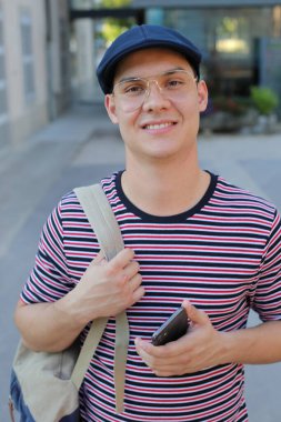  Şık giyinmiş yakışıklı bir gencin portresi, sokakta akıllı telefonlu çanta ve şapka.