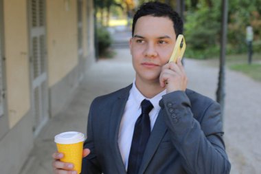 İş adamı kahve içerken telefonda konuşuyor.