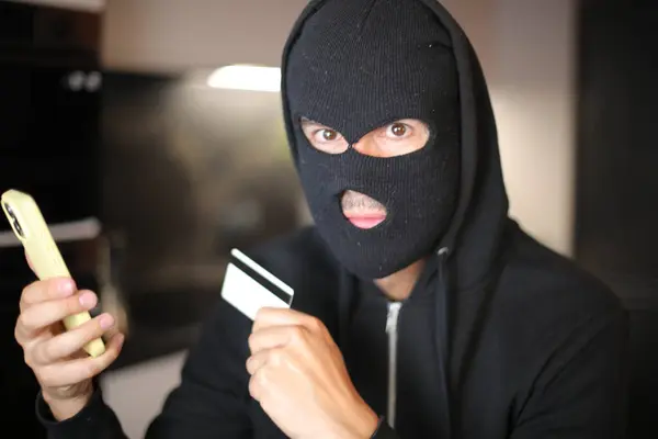 Stock image Concept representing the dangers of an unknown person in s mask holding credit card 