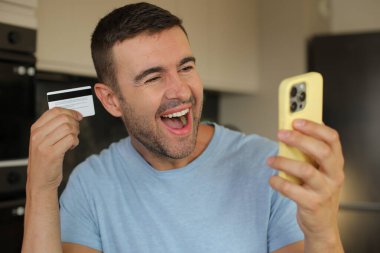 Akıllı telefonu kredi kartıyla tutan mutlu genç adamın portresi.