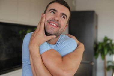 Genç adam evinde kendine sarılıyor.