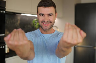 Sıradan beyaz tişört giyen genç ve yakışıklı bir adam kamerayı işaret ederek gülümsüyor.. 