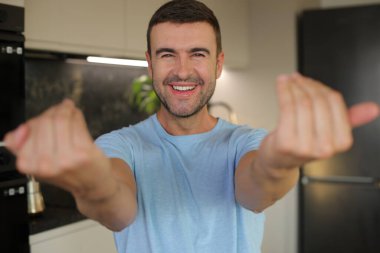 Sıradan beyaz tişört giyen genç ve yakışıklı bir adam kamerayı işaret ederek gülümsüyor.. 