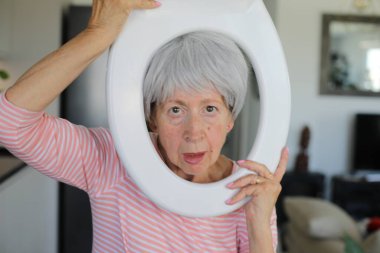 Kıdemli komedyen yüzünün etrafında tuvalet parçası tutuyor.