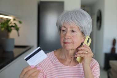 Telefon görüşmesi sırasında kredi kartı tutan şüpheli görünen son sınıf öğrencisi bir kadın.