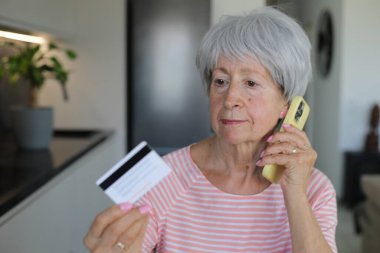 Telefon görüşmesi sırasında kredi kartı tutan şüpheli görünen son sınıf öğrencisi bir kadın.